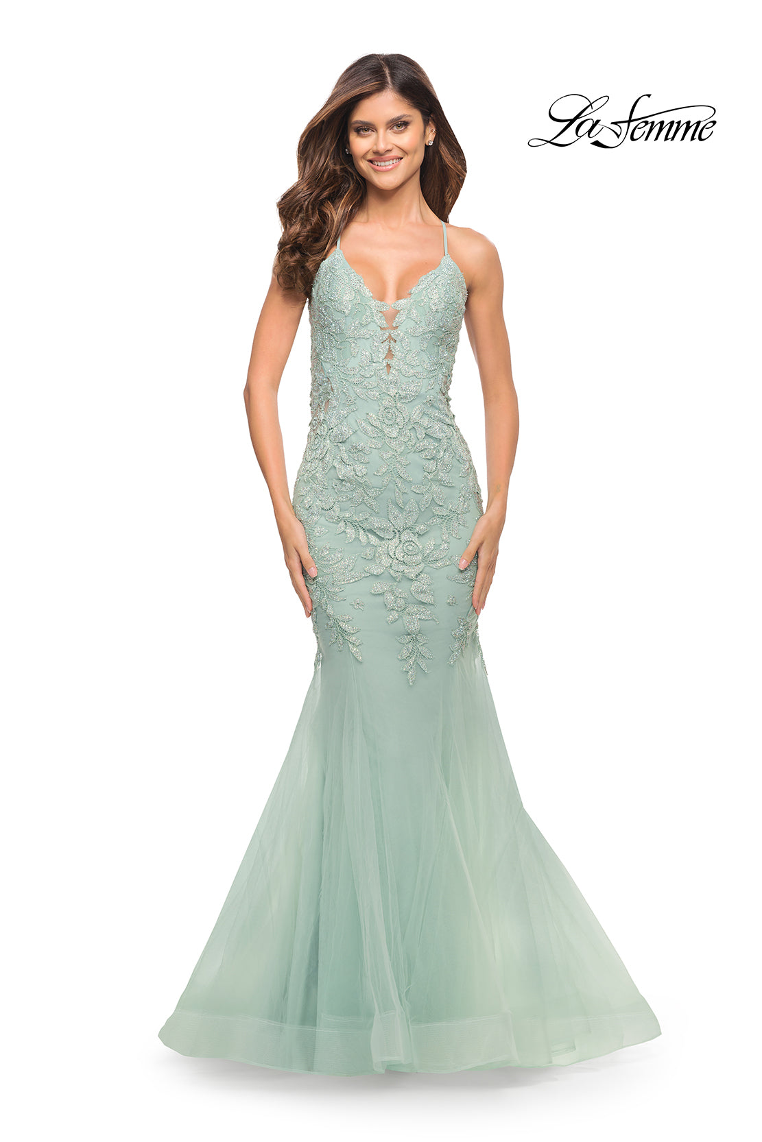 A woman smiles against a plain white background wearing the Backless Long Lace Mermaid Prom Dress by La Femme in light green, featuring floor-length lace, spaghetti straps, and a mermaid silhouette. The 