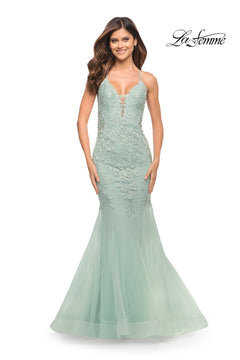 A woman smiles against a plain white background wearing the Backless Long Lace Mermaid Prom Dress by La Femme in light green, featuring floor-length lace, spaghetti straps, and a mermaid silhouette. The "La Femme" logo appears in the top right corner.