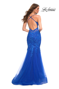 A woman models the Backless Long Lace Mermaid Prom Dress by La Femme, featuring royal blue lace, a floor-length mermaid skirt, crisscross straps, and an open back. The La Femme logo is displayed in the top right corner.