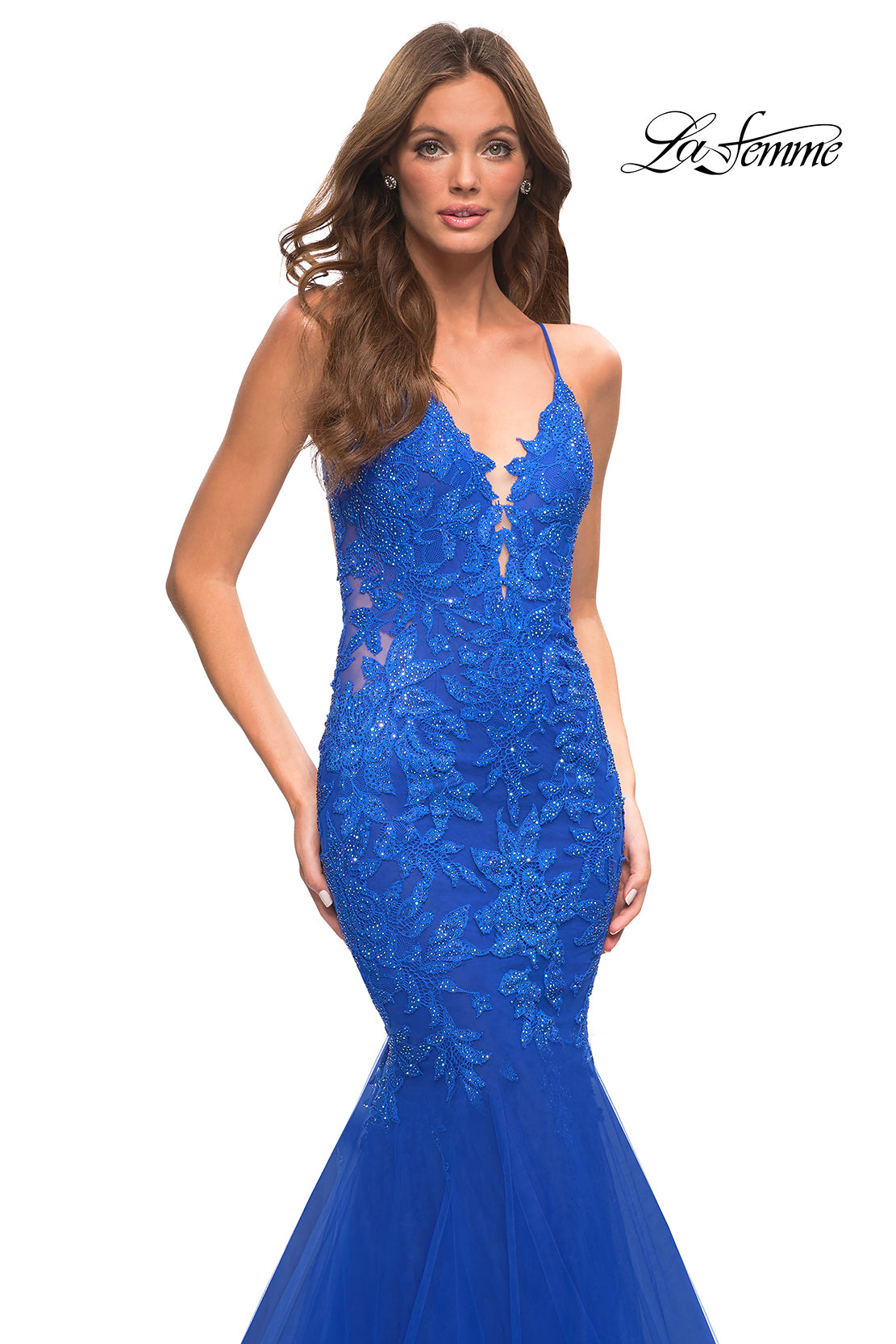 A woman wears the Backless Long Lace Mermaid Prom Dress by La Femme, a fitted, sleeveless royal blue gown with floral lace details and a plunging neckline. The La Femme logo appears in the top right corner.