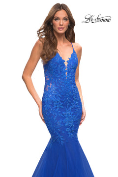 A woman wears the Backless Long Lace Mermaid Prom Dress by La Femme, a fitted, sleeveless royal blue gown with floral lace details and a plunging neckline. The La Femme logo appears in the top right corner.
