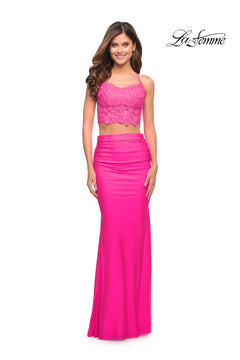 A woman smiles in front of a white background, wearing the Neon Pink Two-Piece Long La Femme Prom Dress with a lace crop top and fitted skirt.