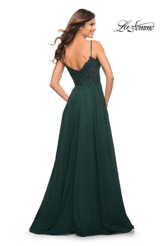 Woman in a dark green La Femme Long A-Line Prom Dress with a sheer bodice and thin straps, facing away; "La Femme" logo appears in the upper right corner.
