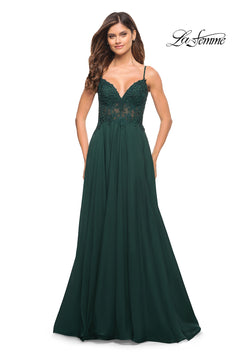 A woman wears the La Femme Long A-Line Prom Dress with a dark green flowing skirt, sheer lace bodice, and thin straps. The La Femme logo is displayed in the upper right corner.