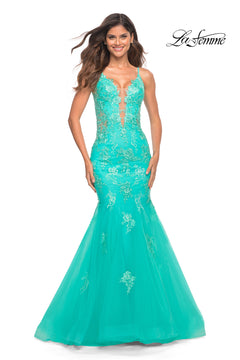 A woman wears the Aqua Blue Long Lace Prom Dress: La Femme 30675, featuring floral embroidery, a sheer bodice, thin straps, and a mermaid silhouette, standing against a white background.