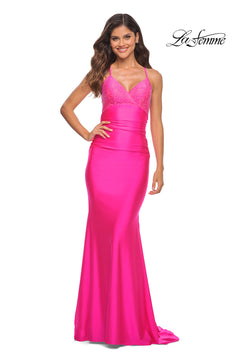 A woman smiles against a white background in the Neon Pink Jersey La Femme Dress 30688, a floor-length gown with an embellished bust, thin straps, fitted bodice, slight train, and elegant lace-up back.