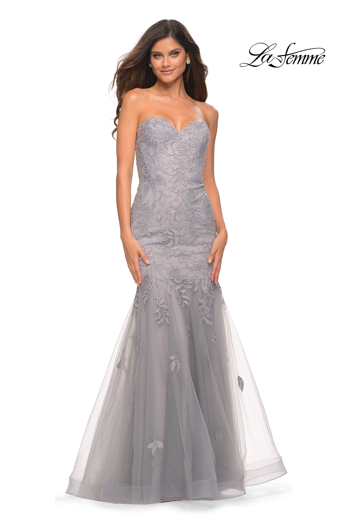 A woman models the Sheer-Back La Femme Strapless Mermaid Prom Dress in silver-grey, with lace accents, a corset back, and tulle skirt. She stands against a white background as 