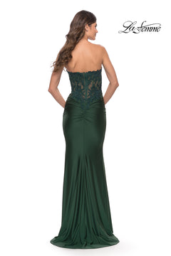 A woman models the Sheer-Lace-Bodice La Femme Strapless Prom Dress in dark green, featuring lace bodice details. Photographed from the back, with the "La Femme" logo in the top right corner.