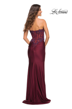 A woman faces away in the Sheer-Lace-Bodice La Femme Strapless Prom Dress, featuring elegant lace details on the bodice. The "La Femme" logo is visible in the upper right corner.