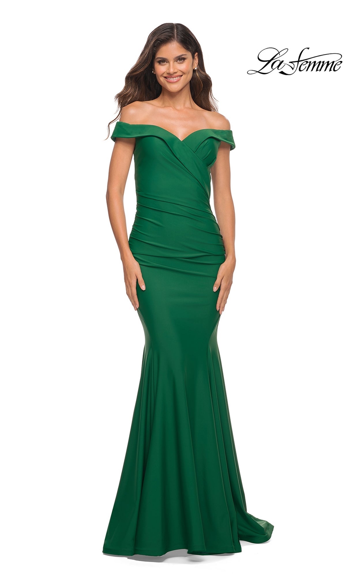 A woman poses and smiles in the fitted, floor-length green La Femme Off-the-Shoulder Long Formal Prom Gown against a white background. The 