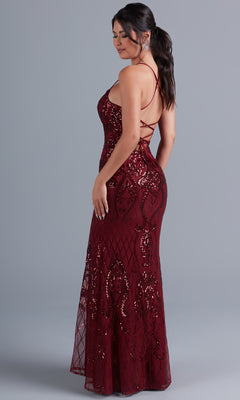 A woman poses against a gray background wearing the PromGirl Statement-Back Long Sequin Prom Dress—a floor-length, burgundy gown with spaghetti straps and a striking open back.