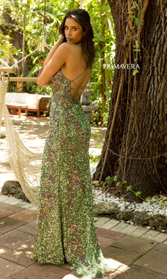 A woman stands outdoors in a V-Neck Sequin Long Prom Gown with lace-up back, surrounded by lush greenery, a tree, and patio furniture for an elegant scene.