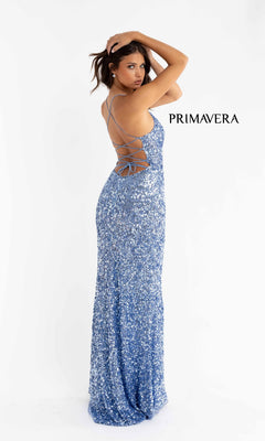 A woman wears the Strappy-Back Pastel Long Sequin Prom Dress 3290, a sparkly blue, backless gown with crisscross straps, posing against a plain white background. The word "PRIMAVERA" appears beside her.