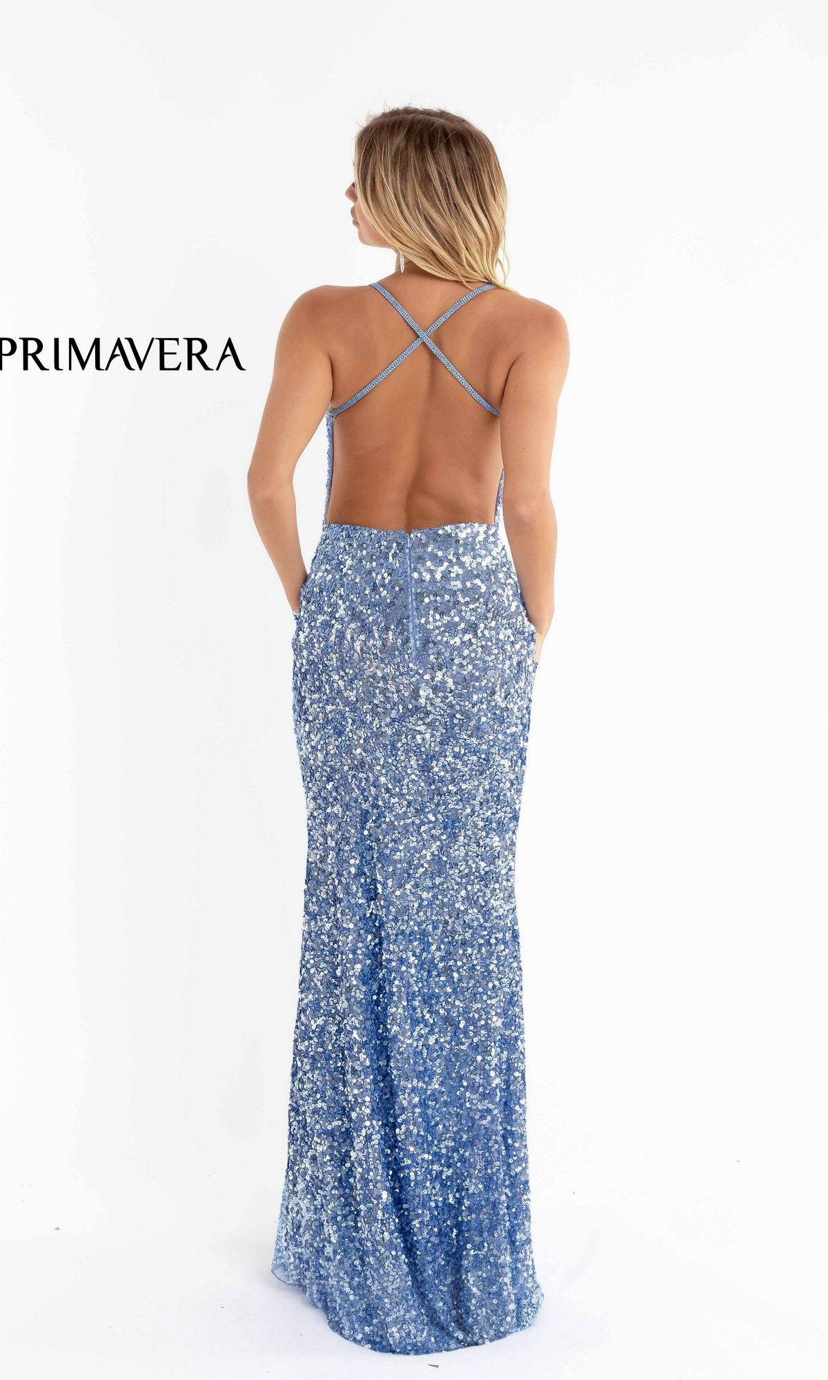 A woman stands facing away, wearing a floor-length, blue Deep V-Neck Long Sequin Prom Dress with a slit and crisscross straps. 