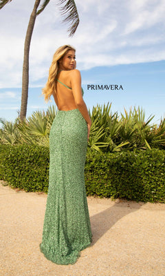 A woman with long blonde hair wears the Open-Back Bright Long Sequin Prom Dress 3291B, standing outdoors near greenery and palm trees under a blue sky. "PRIMAVERA" appears in the background.