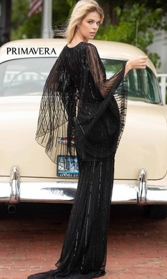 A woman in a Dramatic Sheer-Long-Sleeved Long Formal Dress 3672 poses in front of a vintage beige car, with "PRIMAVERA" displayed in the top left corner.