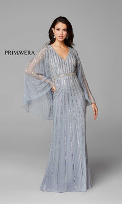 A woman models the Dramatic Sheer-Long-Sleeved Long Formal Dress 3672—silver, sequined, and floor-length with sheer sleeves—against a gray background. “PRIMAVERA” is displayed on the left.