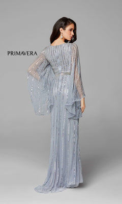 A woman poses with her back to the camera in a light blue Dramatic Sheer-Long-Sleeved Long Formal Dress 3672, featuring beaded details and flowing sheer sleeves, against a plain gray background. "PRIMAVERA" appears on the left.