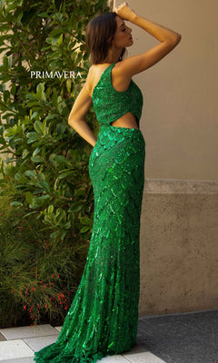 A woman stands outdoors near a wall and greenery, wearing the Primavera 3729 One-Shoulder Long Sequin Prom Dress in green with a side cutout.
