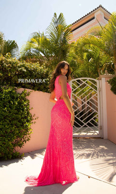 A woman in a floor-length, hot pink one-shoulder gown stands outdoors by a pink wall and white gate with palm trees behind her. "PRIMAVERA" appears, referencing the stunning Primavera 3729N Bright One-Shoulder Sequin Prom Dress.