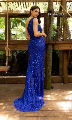 A woman in the Primavera 3729 One-Shoulder Long Sequin Prom Dress stands on a wooden deck, facing backward and looking over her shoulder, with lush greenery in the background.