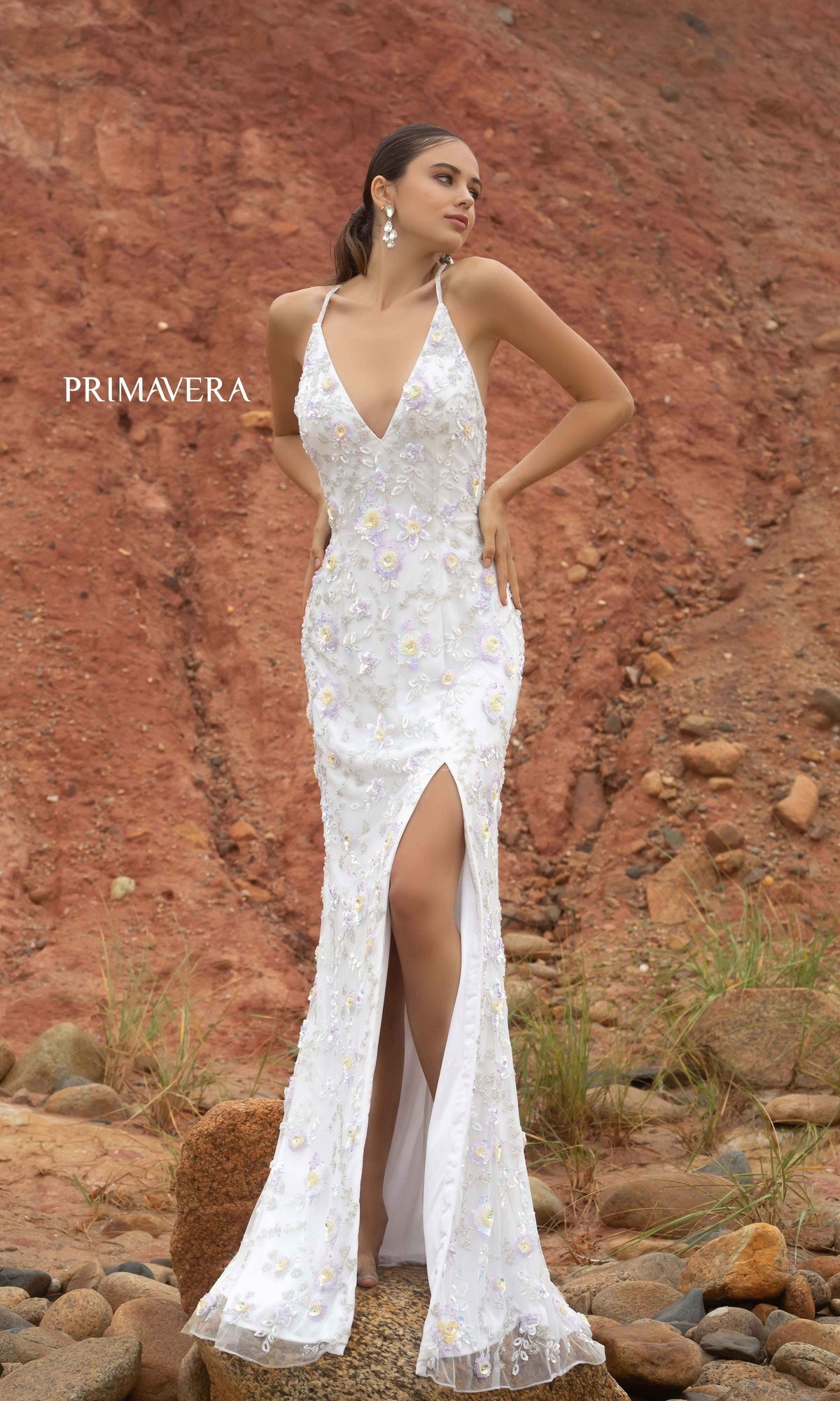 A woman stands on rocky ground in the Primavera 3731 Sequin-Print Long Formal Prom Dress, featuring floral embroidery, a high slit, and a sleeveless design. 