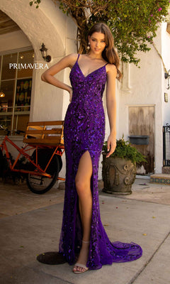 A woman poses outdoors by a planter and orange bike, wearing the Open-Back Primavera 3749 Long Sequin Prom Dress—a sleeveless, deep purple gown with sequins and a thigh-high slit.