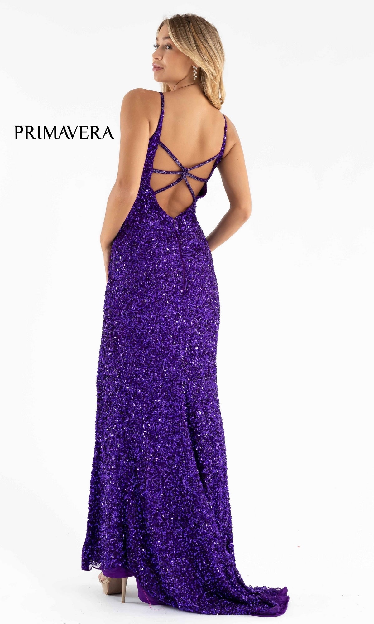 A woman stands with her back to the camera in the Primavera Dark Sequin Long Prom Dress 3792D, a stunning purple gown with a strappy open back. The word 
