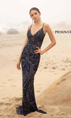 A woman wears the Primavera V-Neck Long Sequin Prom Dress 3793D in dark blue, standing on a sandy beach with rocks and fog in the background.