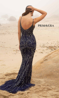 A woman in a navy blue Primavera V-Neck Long Sequin Prom Dress 3793D stands on a sandy beach facing away, hand on her head. "PRIMAVERA" appears in the background.