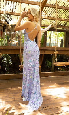 Wearing the Beaded Butterfly Long Prom Dress by Primavera 3901, a woman stands on a wooden deck in a garden-like setting, her long designer gown adorned with delicate light purple floral embroidery.