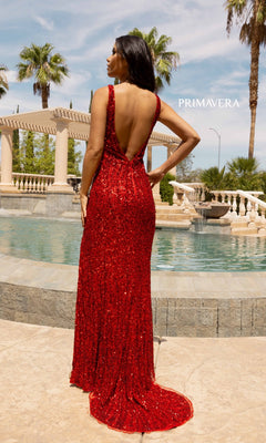 A woman wearing the Open-Back Long Sequin Prom Dress 3912 stands by a fountain, facing away, with palm trees and a pergola in the background.