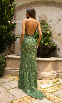 A woman stands outdoors in front of a fountain, wearing the Primavera 3913 Backless Long Sequin Prom Dress featuring a green hue, sparkling embellishments, and a low open back.