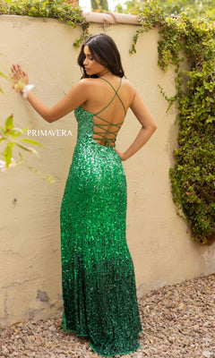 A woman stands outdoors in a Long Ombre Sequin Prom Dress with an open back. Green vines climb the wall behind her, and stones cover the ground beneath her feet.