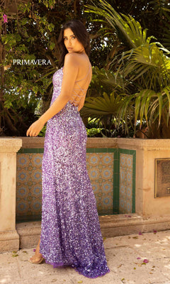 A woman stands outdoors near a tiled wall and lush plants, wearing the Long Ombre Sequin Prom Dress with Open Back. "PRIMAVERA" appears in the background, highlighting her sparkling formal look.