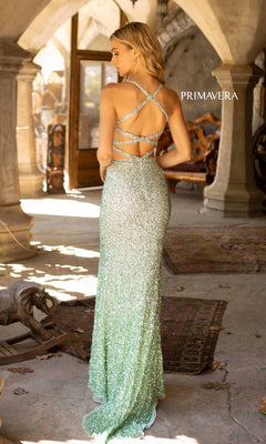 A woman stands indoors in the Primavera 3922 Sequin Ombre Long Prom Dress, featuring sparkling light green sequins, crisscross straps, and a backless design as she faces away from the camera.
