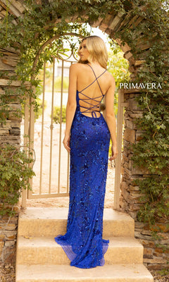A woman in the Strappy-Back Sequin Long Prom Dress 3931, featuring blue sequins and crisscross straps, stands on stone steps before an arched garden gate.