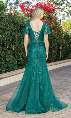 A woman with long blonde hair wears the Sequin-Embellished Long Cape-Sleeved Formal Gown, standing on a paved path near greenery and red flowers.
