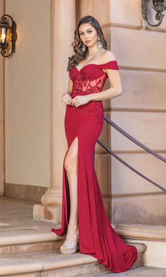 A woman in the Sheer-Bodice Off-the-Shoulder Long Prom Dress, featuring a corset-style bodice and lace details, stands on stone steps beside a wall with an iron lantern.