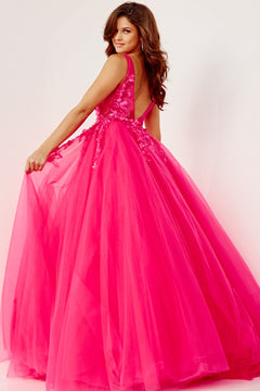 A woman in a bright pink Jovani Tulle Prom Ball Gown with floral appliques, featuring a floor-length ball gown silhouette and deep V back, stands against a plain background, looking over her shoulder while holding part of the dress.