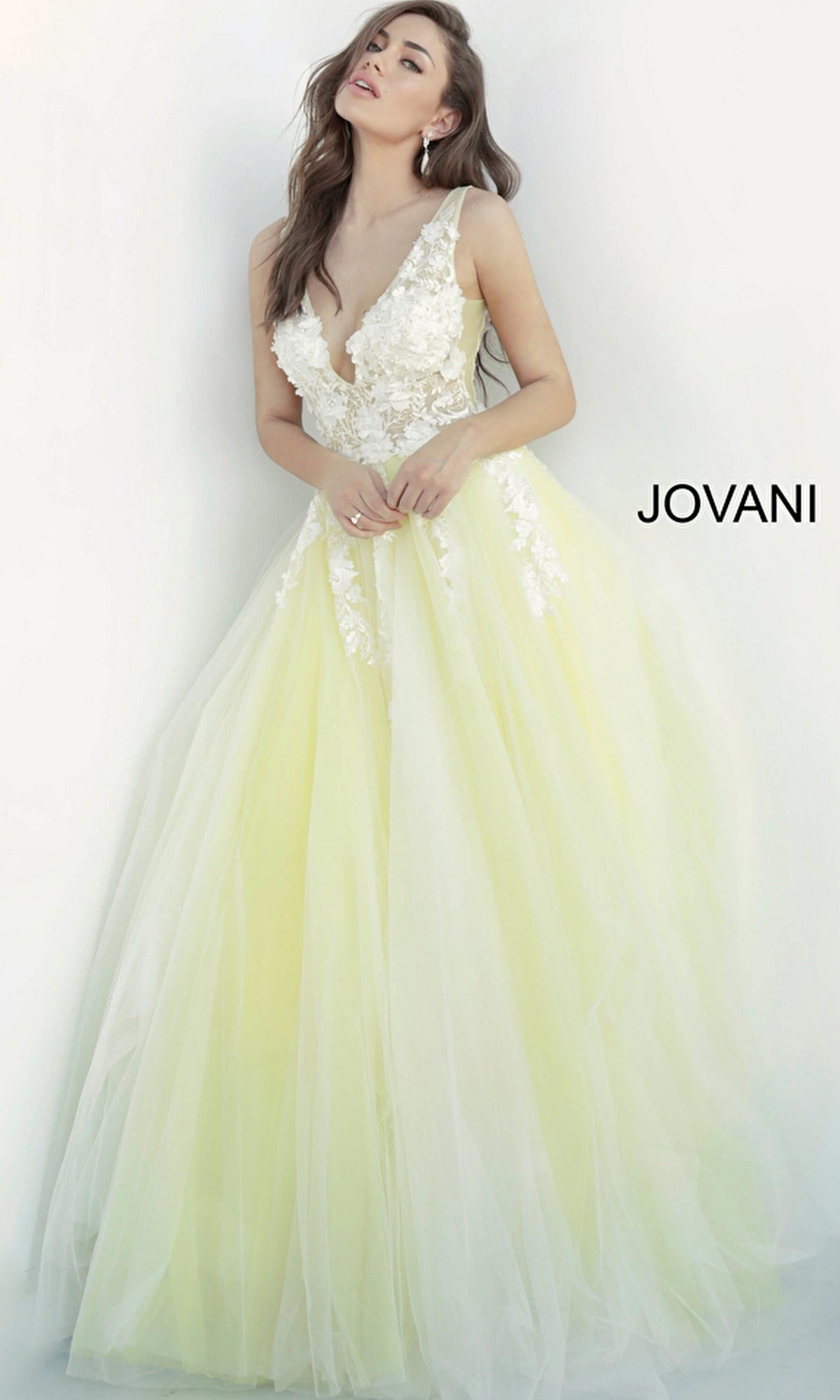 A woman wears the Jovani Tulle Prom Ball Gown with Floral Appliques, featuring a light yellow hue, fitted floral lace bodice, delicate floral appliqués, and flowing tulle skirt. 