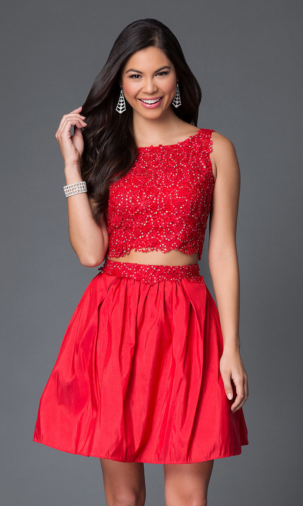 Young woman in a Two-Piece Lace-Bodice Short Party Dress featuring a sleeveless red lace top and matching skirt, posed against a plain gray background.