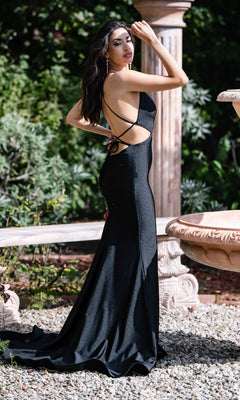 A woman poses outdoors near a stone fountain and greenery, wearing the Atria Sexy Cut-Out Long Black Formal Dress 6823H with one arm raised and the other on her hip.