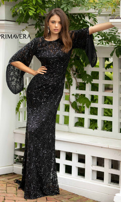 A woman wears the Long Bell Sleeve Beaded Evening Gown 9713 in black, featuring sheer bell sleeves, as she stands before a white lattice fence and lush greenery.