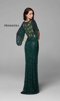 A woman models the Long Bell Sleeve Beaded Evening Gown 9713—a floor-length, dark green dress with sheer bell sleeves and a partially transparent back. The plain light gray background features "PRIMAVERA" text on the left.