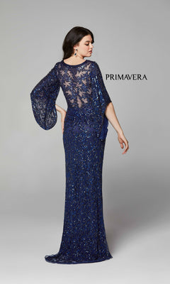 A woman faces away in the Long Bell Sleeve Beaded Evening Gown 9713, a floor-length, dark blue dress with sheer lace sleeves and back. "PRIMAVERA" appears to her right.