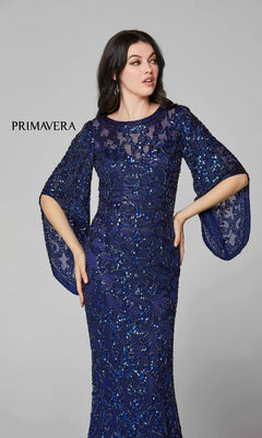 A woman models the Long Bell Sleeve Beaded Evening Gown 9713, a floor-length navy dress with sheer wide bell sleeves, against a plain light gray background. "PRIMAVERA" is displayed on the left.