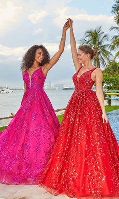 Two women wearing pink and red Colette Designer Prom Sequin & Glitter Ball Gowns stand hand in hand by the water, smiling beneath palm trees with a city skyline in the background.