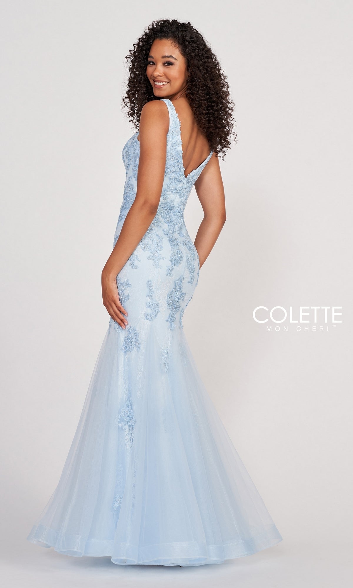 A woman wears the Light Blue Long Mermaid Prom Dress by Colette, featuring beaded lace details, as she poses looking over her shoulder.