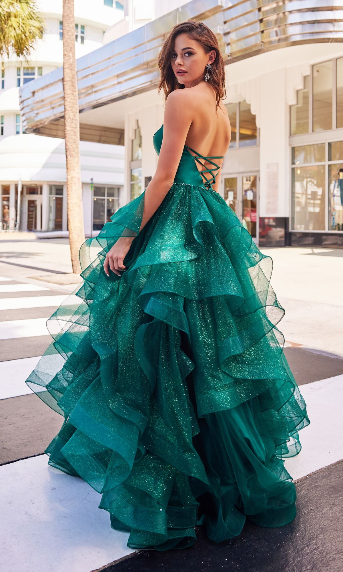 A woman in the Colette Glitter-Tulle Layered Long Prom Ball Gown stands outdoors on a crosswalk, looking back over her shoulder.